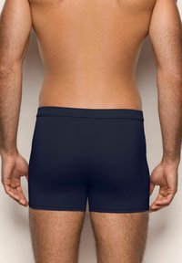 Șorturi de baie bleu marin, confecționate dintr-un material neted, având un design minimalist, cu o talie sigură și fără logo-uri vizibile.