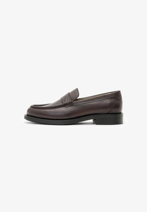 Mocasines de cuero marrón oscuro con un acabado suave, tacón bajo apilado y detalle de ranura en la parte delantera. Diseño elegante con suela negra resistente.