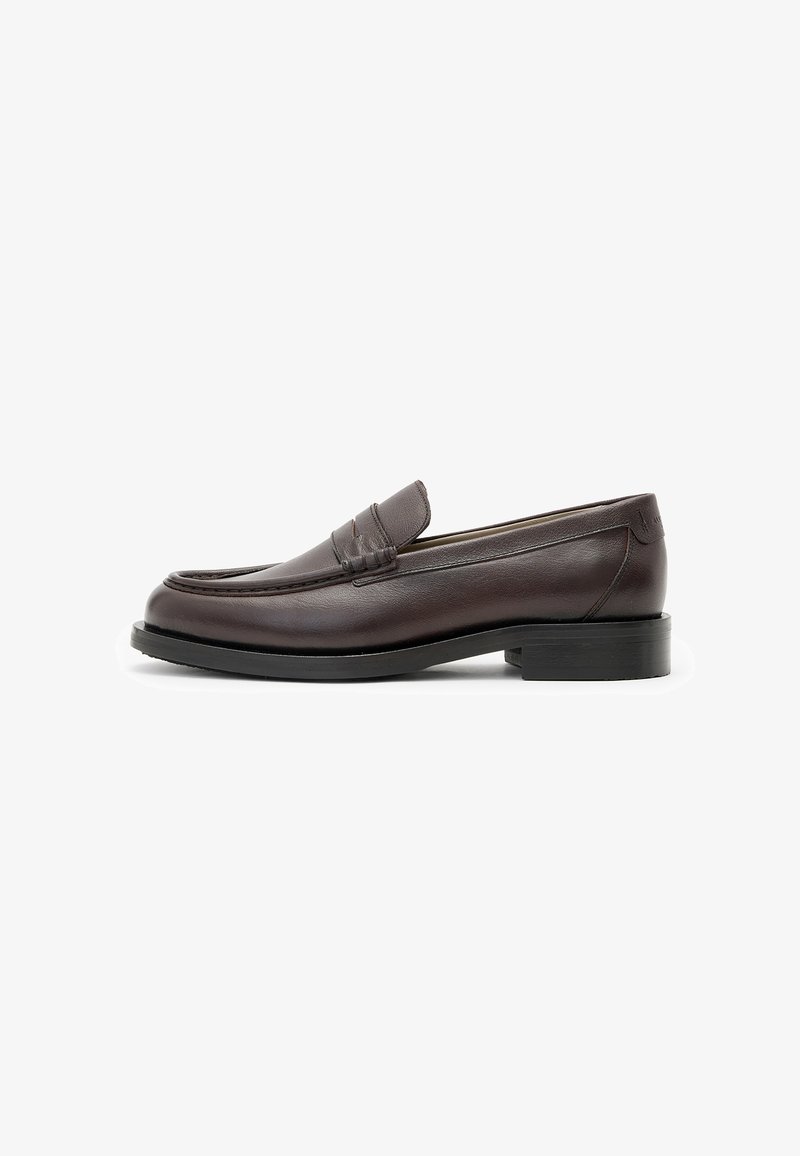 Mocasines de cuero marrón oscuro con un acabado suave, tacón bajo apilado y detalle de ranura en la parte delantera. Diseño elegante con suela negra resistente.