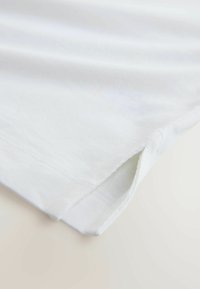 Bílé bavlněné tričko s hladkou texturou, srolovanými lemy rukávů a bočními rozparky. Jednoduchý design a nenápadné provedení.