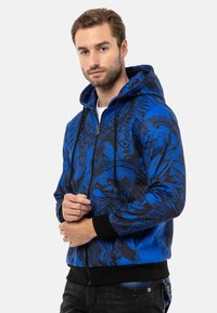Blaue Zip-Hoodie mit schwarzem Grafikdesign, verstellbarem Kordelzug und gerippten Bündchen. Glattes Material mit lässiger Passform.