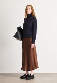 Marineblå turtleneck-genser, brun midtbl Ång-skirt, svarte loafers, holder en svart lærveske. Glatte teksturer, enkelt design, nøytrale farger.