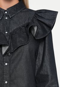 Knarvet skjorte i mørkeblå med en blank finish, med volangdetaljer foran og spiss krage, festet med sølvknapper.