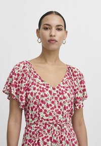 Floral dress with a V-neckline and flutter sleeves. Made from lightweight fabric, featuring red and green flower patterns on a cream background.
