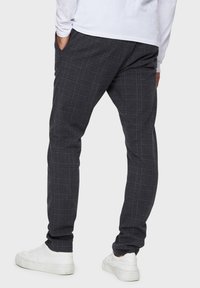 Dark gray plaid trousers featuring side pockets, a relaxed fit, and soft fabric. Paired with white sneakers for contrast.