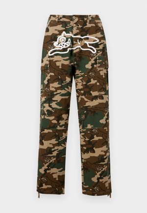 Camo cargo bukser i brun og grøn med et stort hvidt grafisk tryk af en tegneseriefigur og flere lommer med mønstrede detaljer.