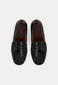 Mocassins en cuir noir à finition lisse, ornés d’une chaîne décorative et d’un intérieur marron contrastant. Design classique avec un embout arrondi.