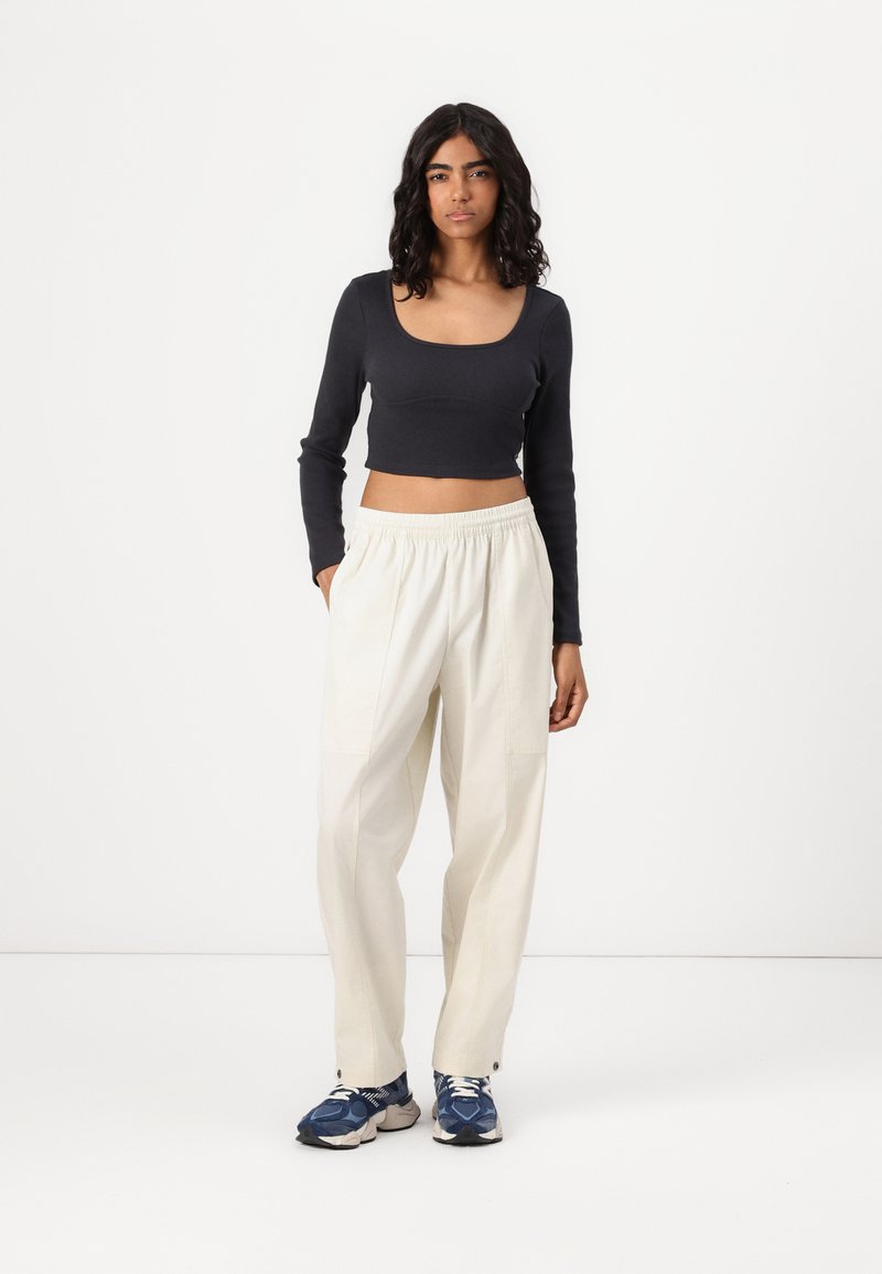 Haut noir à manches longues cropped avec un décolleté carré, assorti à un pantalon blanc ample avec des poches latérales et une taille élastique. Baskets bleues.