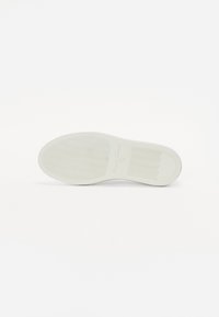 Semelle de chaussure blanche avec une surface texturée comprenant des motifs en vagues et un bout lisse et arrondi. Marque en relief près du talon.