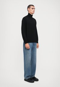 Svart polotröja i mjukt material, kombinerad med ljusblå, vida denimjeans och svarta snörskor. Enkel, modern stil.