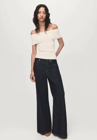 Romantische crèmekleurige top zonder schouderbanden met een aansluitend ontwerp, gecombineerd met wijde, donkere denim broek. Zachte texturen en contrasterende kleuren.
