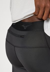 Leggings sportivi neri con una vestibilità aderente, dotati di una fascia in vita texturizzata e di una piccola tasca con zip sul retro. Finitura in tessuto liscia.