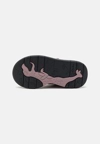 Podeszwa buta z czarnym i purpurowym wzorem dinozaura na spodzie, pokazująca wypukłą teksturę i nazwę marki Clarks.