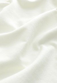 Biały bawełniany materiał o gładkiej teksturze, z delikatnymi zagnieceniami i fałdami, podkreślający jego lekkość i miękkość.