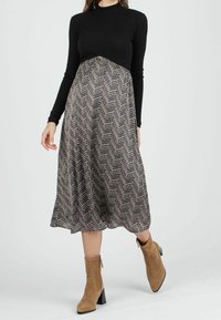 Haut noir à manches longues côtelé avec un corsage ajusté, se transformant en une jupe à motifs en chevron marron et blanc, associée à des bottines taupe.