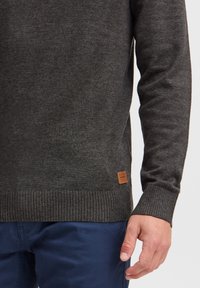 Dark gray knit sweater with ribbed cuffs and hem. Includes a small brown leather label on the lower side. Soft texture, fitted design.