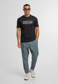 Svart bomull t-shirt med "Sergio Tacchini" logotyp, kombinerad med grå träningbyxor, bärs med vita sneakers. Släta texturer och avslappnad passform.