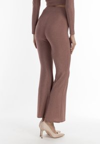 Pantaloni svasati a vita alta, rigati e in oro rosa con una leggera lucentezza. Adatti in vita, si allargano dal ginocchio. Abbinati a tacchi nudi.