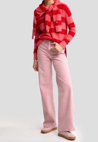 Červeno-růžový pruhovaný svetr s uvázaným límcem, spárovaný se světle růžovými kalhotami s širokými nohavicemi a růžovými botami s béžovou podrážkou. Neformální outfit.