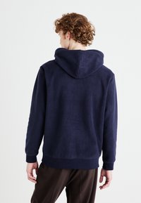 Hanorac din fleece de culoare bleumarin, cu glugă ajustabilă, manșete și tiv ribatate; textură moale, croială lejeră și design simplu.