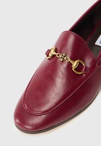 Burgundia nahast loafers, millel on kuldse tooni ahelate kaunistus ja peened õmblused siledal pinnal. Tasane tald ja ümar varvas.