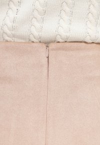 Μπεζ πουλόβερ πλεκτό με καλώδιο πάνω σε ελαστικό ύφασμα ανοιχτό ροζ, με ορατή λεπτομέρεια φερμουάρ στο πίσω μέρος. Ομοιόμορφη λεία υφή.