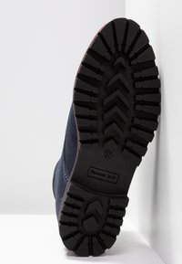 Svart gummisula med ett greppmönster, blått övermaterial och en röd accent längs hälen. Märke "Panama Jack" synligt. Storlek 37.