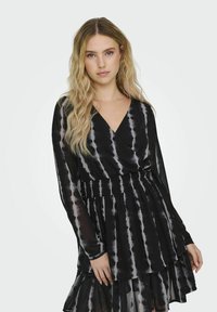 Schwarz- und grau-gebundene Kombination aus Kleid mit langen Ärmeln, V-Ausschnitt und gerafftem Bund. Mit einem geschichteten, fransigen Rock und transparenter Textur.