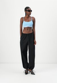 Haut de brassière cropped bleu clair avec la marque Calvin Klein, associé à un pantalon noir ample et des chaussures à talons noirs avec des accents en dentelle.