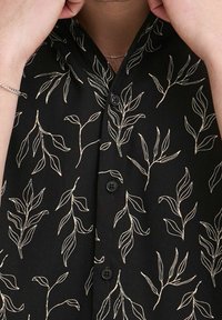 Zwarte overhemden met een bladmotief in crèmekleur. Het shirt heeft een gladde textuur en een kraag met korte mouwen.