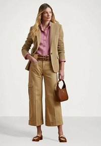 Woman wearing beige wide-leg pants with pockets, a pink button-up shirt, tan blazer, brown belt, brown handbag, and matching loafers.