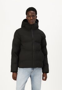 Sort puffjakke med hætte, der har en lynlås foran og en quiltet design; parret med lyseblå jeans. Glat tekstur.