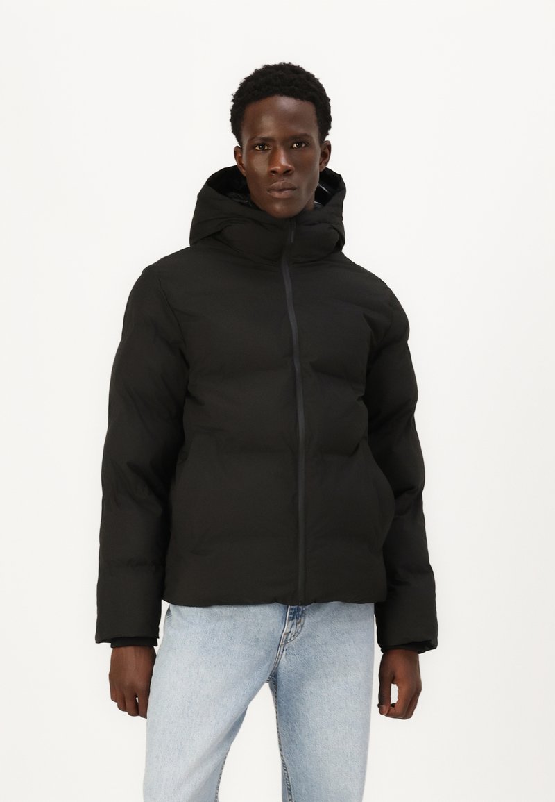 Sort puffjakke med hætte, der har en lynlås foran og en quiltet design; parret med lyseblå jeans. Glat tekstur.