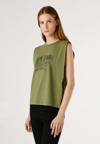 Top senza maniche verde oliva in cotone morbido con scollatura rotonda, caratterizzato da una stampa grafica nera di ali e testo sul davanti.