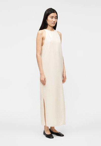 Φόρεμα αμάνικο σε ανοιχτό μπεζ χρώμα με ευθύγραμμη γραμμή, πλαϊνή σχι σμή και λεία υφή. Φοριέται με απλά μαύρα φλατ παπούτσια.