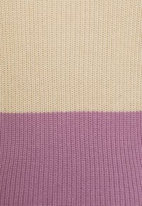 Tessuto lavorato a maglia con la parte superiore orizzontale di colore crema e la parte inferiore viola, che mostra una dettagliata texture del punto.