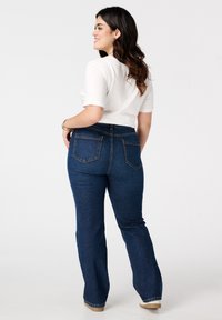 Blauwe flared jeans met achterzakken en zichtbare stiksels, gedragen met een witte top met korte mouwen. Gladde denimtextuur en een medium taille.