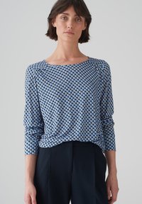 Blau gemustertes Langarmoberteil mit geometrischem Design in Tönen von Blau und Creme. Rundhalsausschnitt und rüschenartige Details an den Schultern.