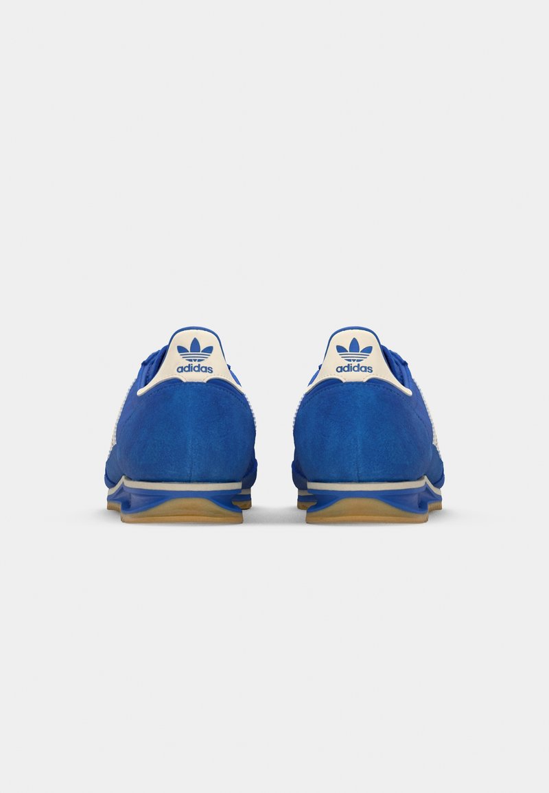 Niebieskie zamszowe buty sportowe z białymi akcentami i logo na pięcie. Teksturowana cholewka, gumowa podeszwa i smukły design zapewniający komfort.