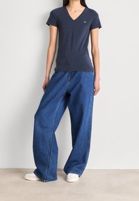 Námořnické tričko s hlubokým výstřihem vyrobené z měkké látky, doplněné volnými modrými džíny. Tenisky jsou bílé plátěné s texturovaným povrchem.