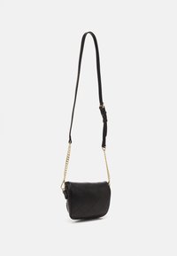 Černá prošívaná kabelka přes rameno s zakřiveným klopem, zlatým řetězem a nastavitelným koženým popruhem, zavěšená na hladkém bílém pozadí.