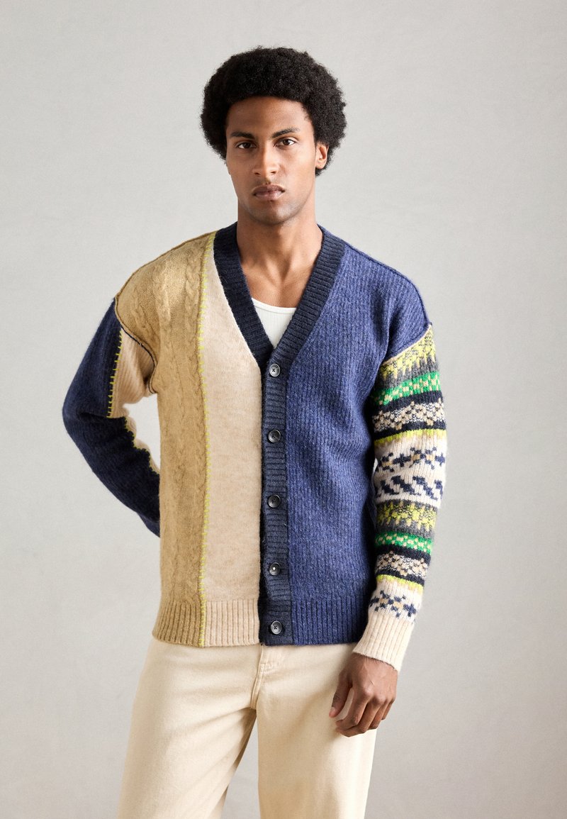 Strikcardigan med en blanding af beige, marineblå og mønstrede ærmer. Har en V-hals, knaplukning foran og tekstureret stof for ekstra varme.