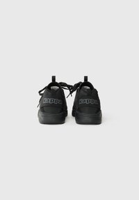Baskets noires de sport avec une finition texturée, arborant un logo Kappa, des lacets ronds et une languette au talon pour un enfilage facile.