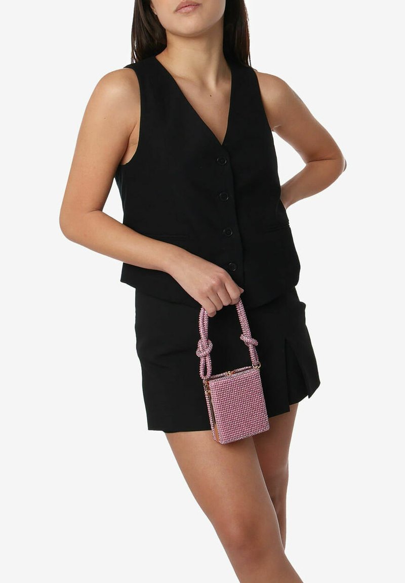 Piccola borsa rosa con superficie testurizzata e manico annodato, abbinata a un top senza maniche nero e pantaloni corti.