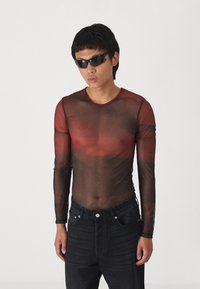 Black sheer long-sleeve shirt with a gradient red design. Worn with dark denim jeans and black sunglasses. Close-fitting, lightweight fabric.