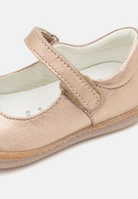 Zapato Mary Jane de color rosa dorado metálico con suela de goma plana, puntera redondeada y una correa ajustable segura en el medio del pie.