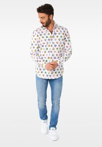 Balta ilgomis rankovėmis marškiniai, puošiami spalvinga animacinių filmų personažų raštu, derinami su šviesiai mėlynomis džinsais ir baltais sportbačiais.