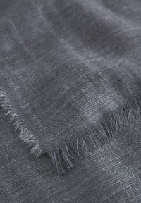 Textil in Dunkelgrau, mit einer weichen, strukturierten Oberfläche und einem dezenten gewebten Muster sowie fransenartigen Kanten. Das Material wirkt leicht und atmungsaktiv.