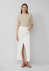 Haut à manches courtes rayé beige et blanc associé à une longue jupe blanche avec une fente à l'avant et une taille nouée, porté avec des sandales marron.
