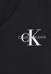 Czarna tkanina z białymi inicjałami "CK" oraz szarym napisem logo "Calvin Klein Jeans" nadrukowanym blisko kołnierza.